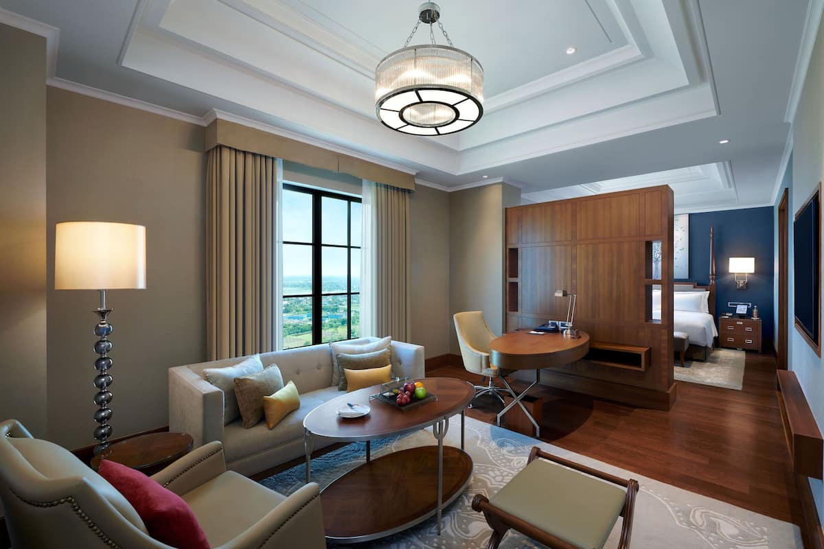 Ein Hotelzimmer mit einer Couch, Sesseln, einem Esstisch, einer Chandelüster und Blick ins Freie.