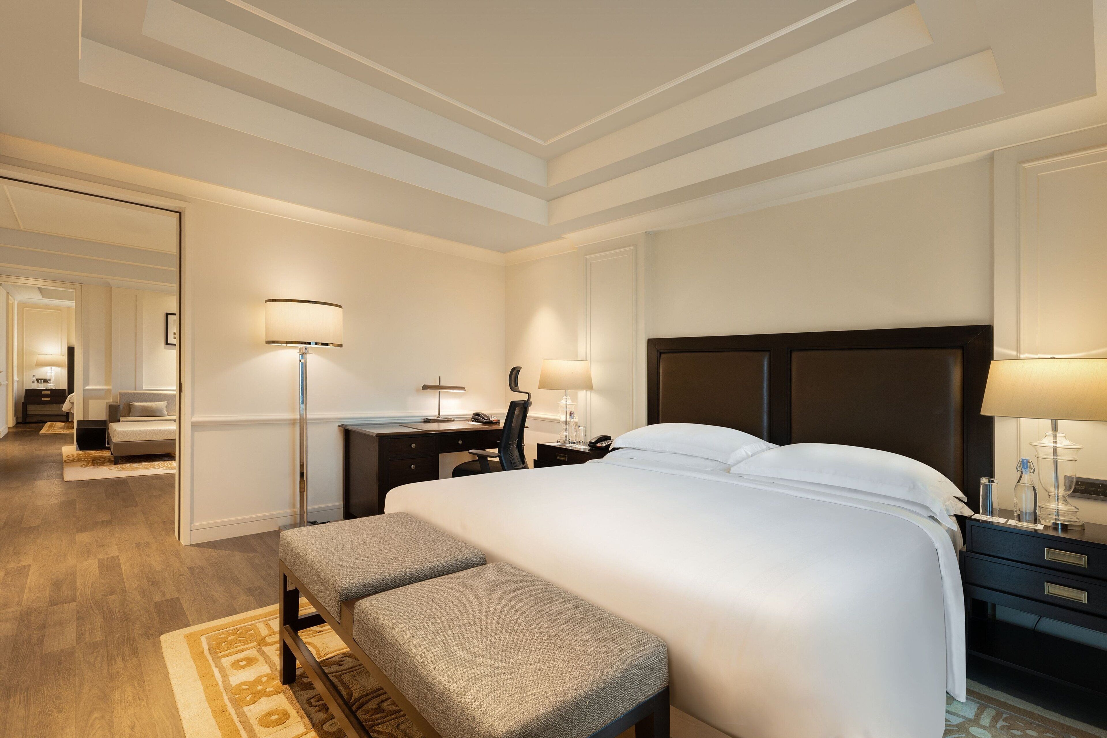 Una habitación de hotel con una cama grande, un escritorio, una silla, un banco y una mesita de noche con lámparas.