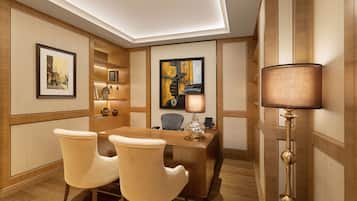 A modern hotel room with a wooden desk, two chairs, a lamp, and framed artwork on the walls.