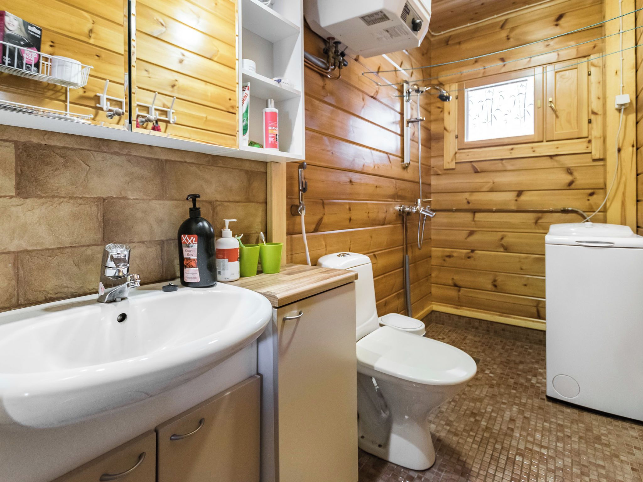 Et badeværelse med træpaneler, håndvask, toilet og brusebad.
