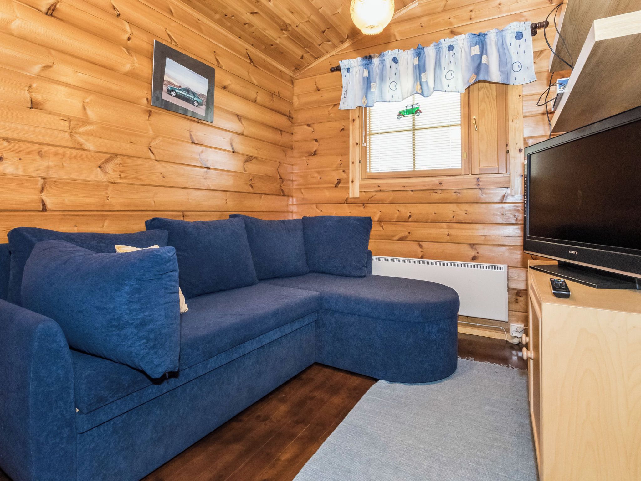 L’intérieur d’un chalet en bois, avec un canapé d’angle, un téléviseur et une fenêtre avec des rideaux.