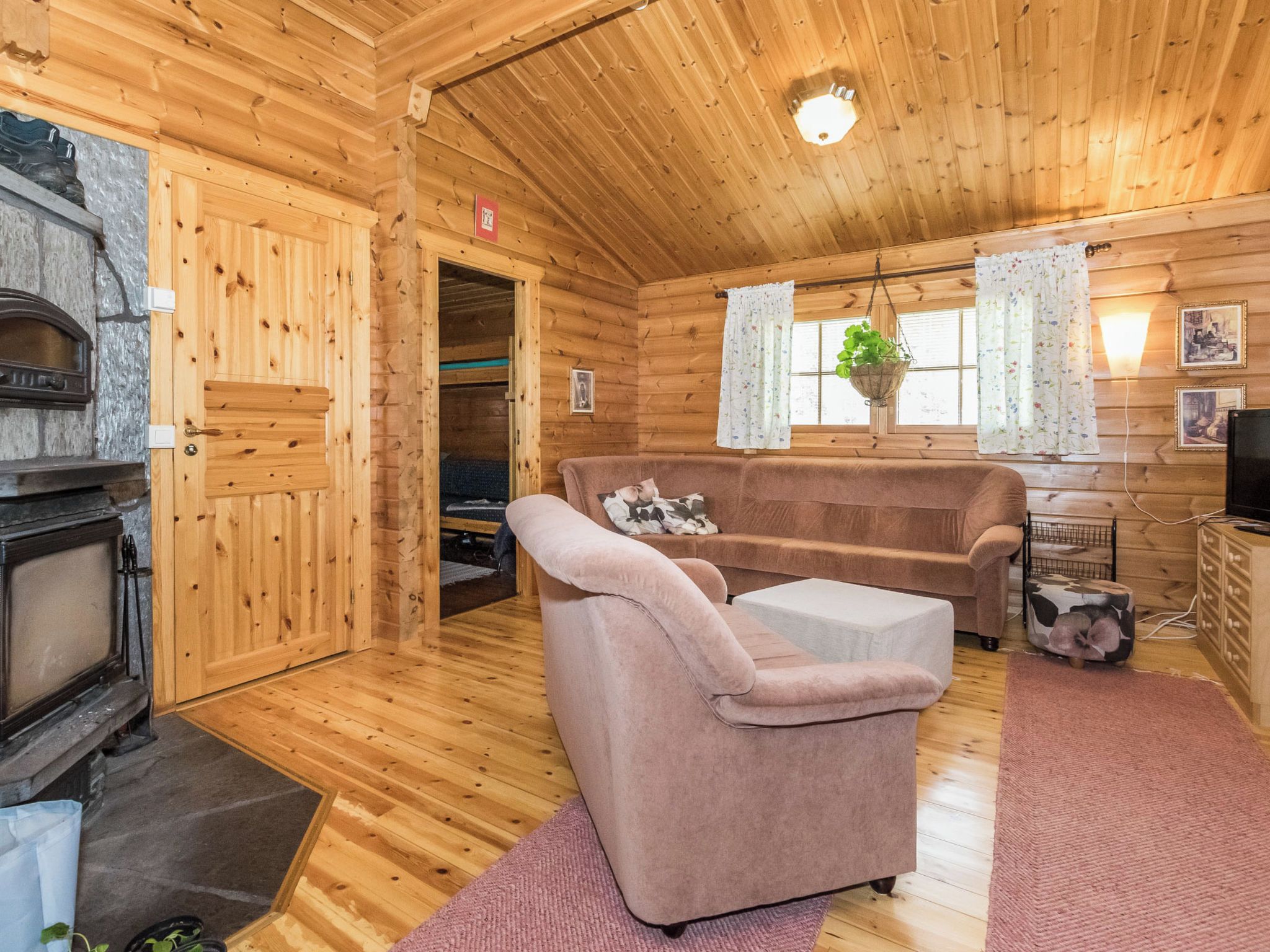 A cozy log cabin interior with a fireplace, a sofa, a chair, and a television.
