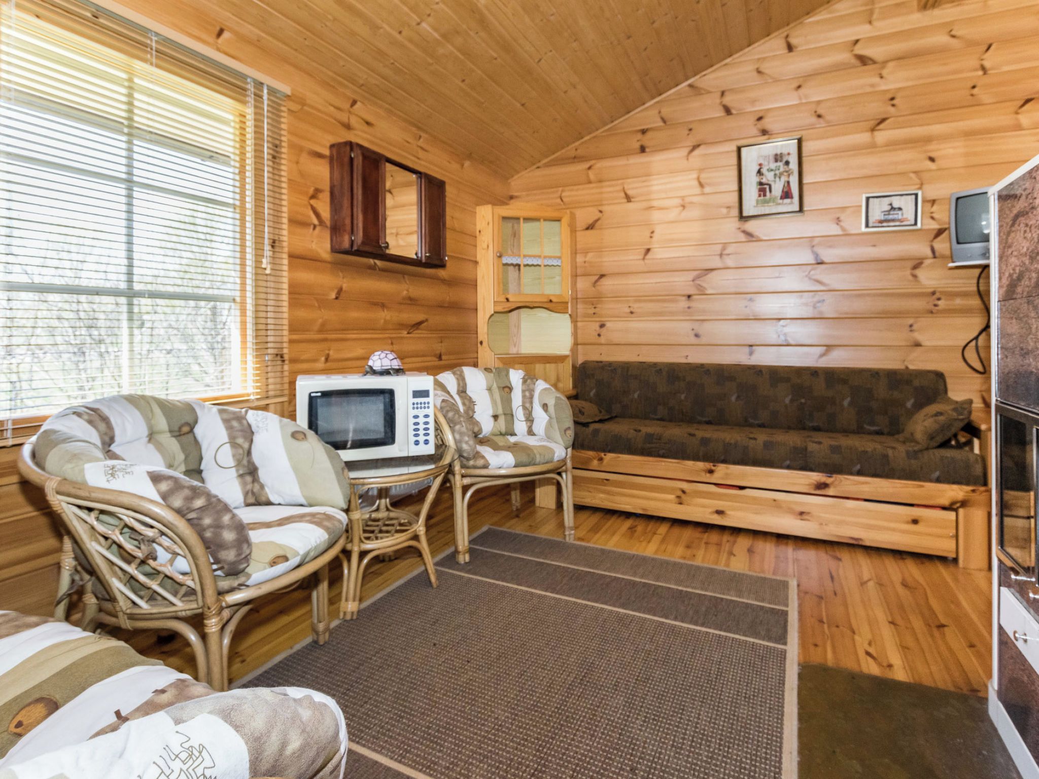 L’intérieur chaleureux d’un chalet, avec un revêtement mural en bois, un canapé, deux fauteuils, une petite table sur laquelle se trouve un four à micro-ondes, et un téléviseur.
