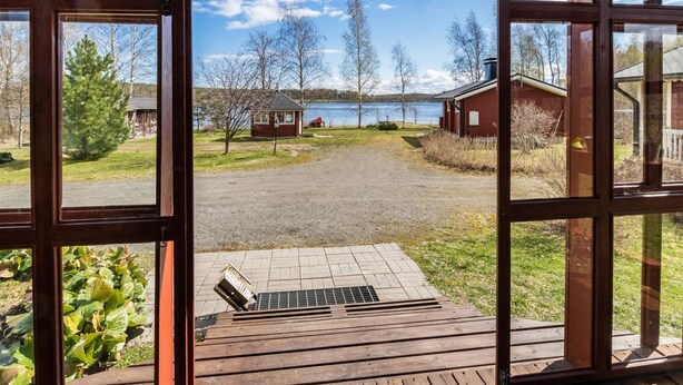 A wooden deck with a metal grate, a gravel path, and a view of a lake with buildings and trees. - Vacation home Eden by Interhome (Laukaa)