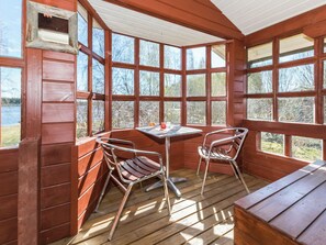 Een houten chalet met een hoektafeltje en twee stoelen, grote ramen en uitzicht op een meer.