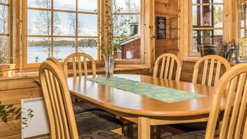 A wooden interior with a dining table, chairs, and a view of a lake.