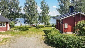 A red cabin with a gravel driveway leading to a lake, surrounded by greenery and trees. - Vacation home Eden by Interhome (Laukaa)