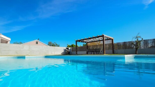 Une piscine d’eau bleue et limpide, dotée d’un espace de repos abrité et d’un mur en béton.