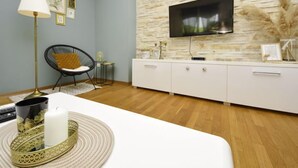 Un salon moderne avec un mur en pierre, un téléviseur à écran plat, un meuble blanc, un fauteuil noir et un plateau décoratif avec une bougie.