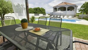 Une terrasse extérieure avec une table et des chaises, une petite plante en pot, et une vue sur une piscine et un bâtiment en arrière-plan.