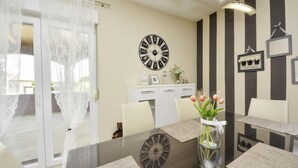 Un espace repas moderne avec une table en verre, des chaises blanches, une horloge et un vase rempli de fleurs.