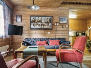Una sala de estar acogedora con detalles de madera, un sofá, un sillón rojo, una mesa y un televisor.