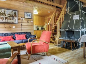 A cozy cabin interior with a wooden interior, a stone fireplace, a sofa, a chair, and a staircase. - Lomamaja 2 by Interhome (Raattama)