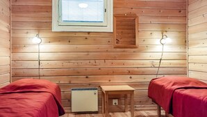 Una habitación tipo cabaña acogedora con dos camas, una mesita, un calentador y dos lámparas de pared.