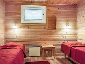 Een kleine, knusse kamer met houten wanden, twee bedden met rode beddengoed, een klein tafeltje, een verwarming en twee wandlampen.