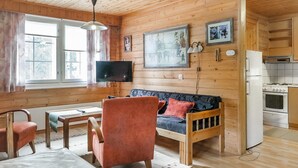 Interior acogedor de una cabaña con techo de madera, un sofá, una mesa de comedor, un televisor y una zona de cocina.