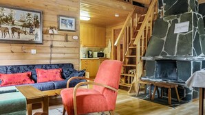 Interior acogedor de una cabaña con detalles de madera, un sofá, un sillón rojo, una chimenea y una escalera.