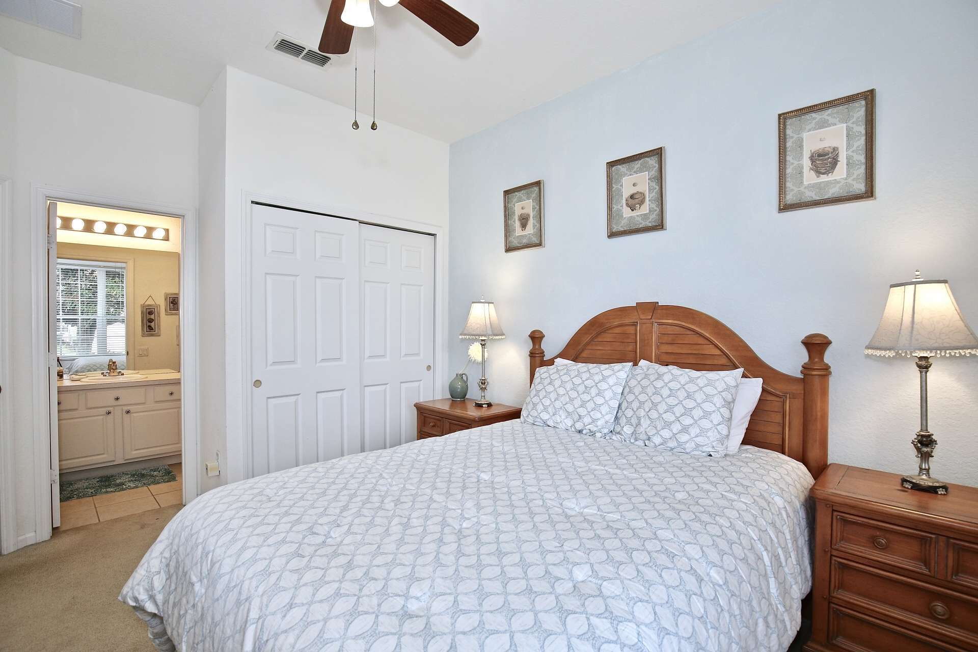 A bedroom with a bed, two bedside tables with lamps, a wooden headboard, and a white door with a mirror.