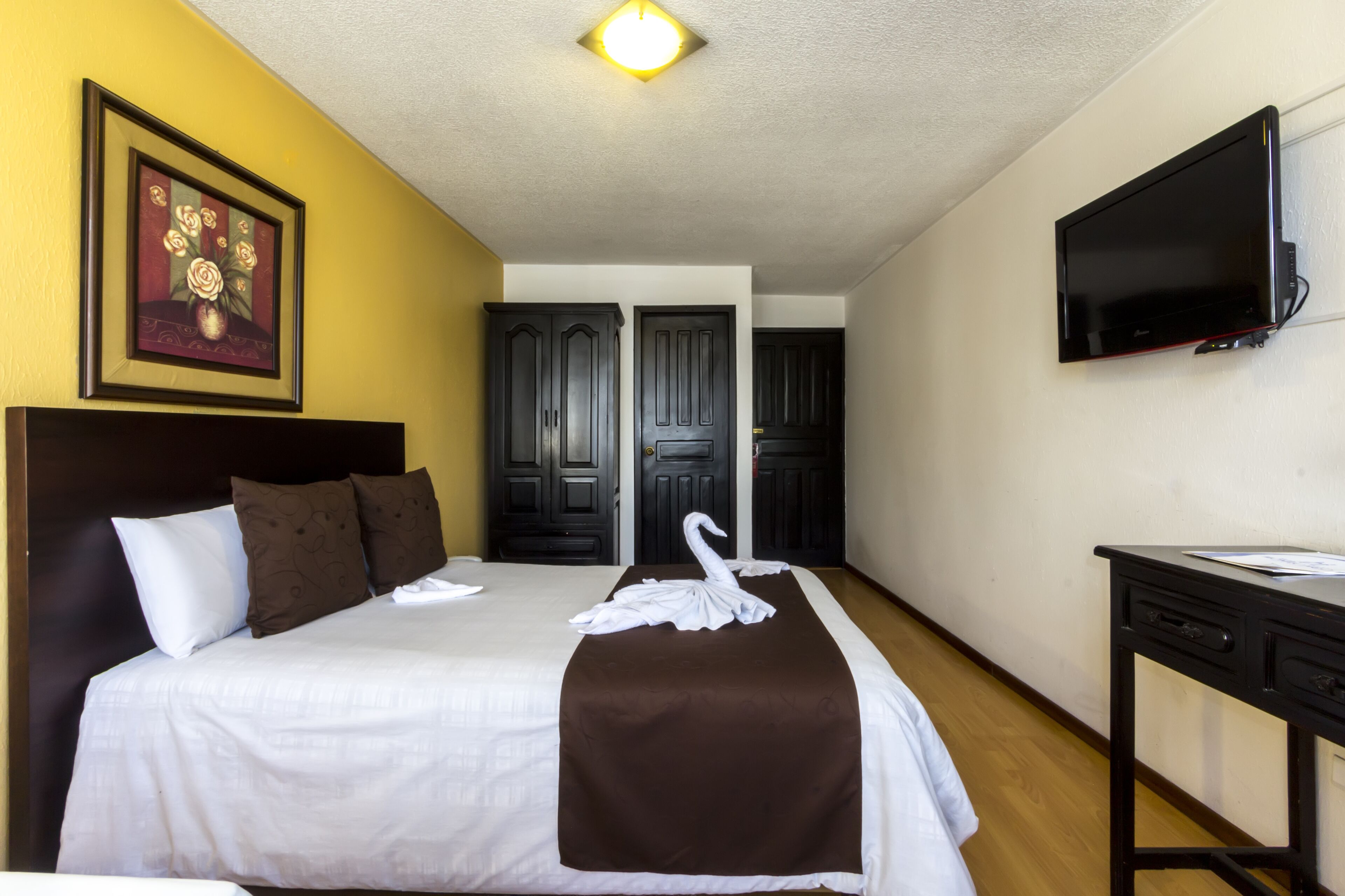 A hotel room with a bed, a TV mounted on the wall, and a door leading to another room.