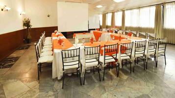 A conference room with a long table and chairs, a projector screen, and a potted plant.