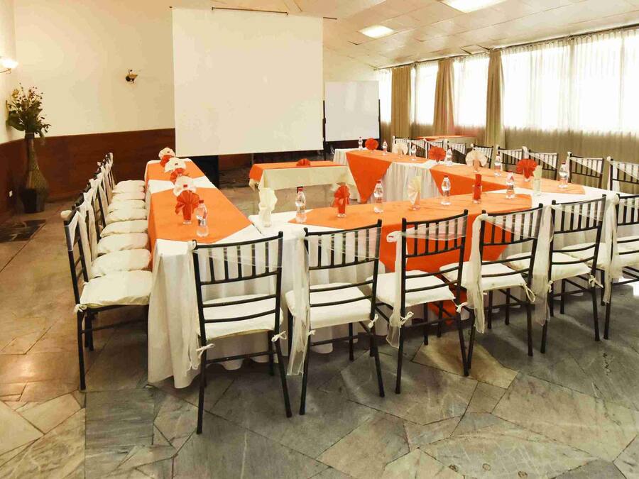 A conference room with a long table and chairs, a projector screen, and a potted plant.