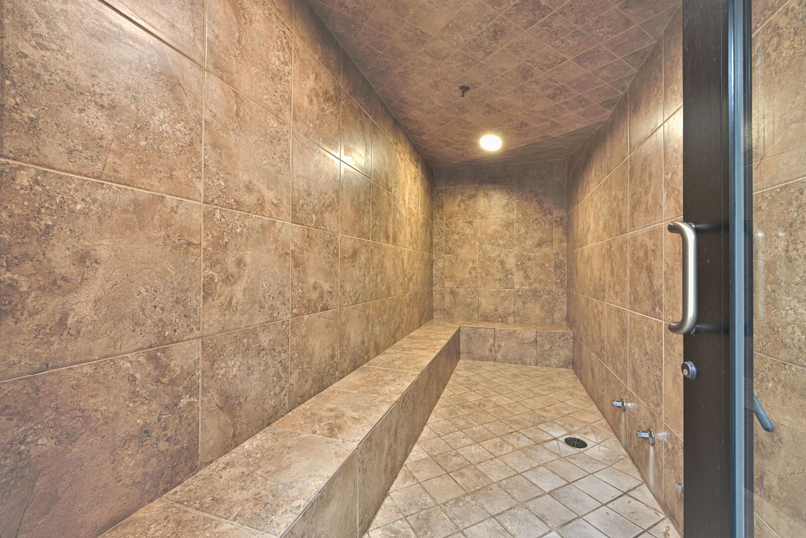 A shower area with tiled walls and floor, a handrail on the right, and a light fixture on the ceiling.