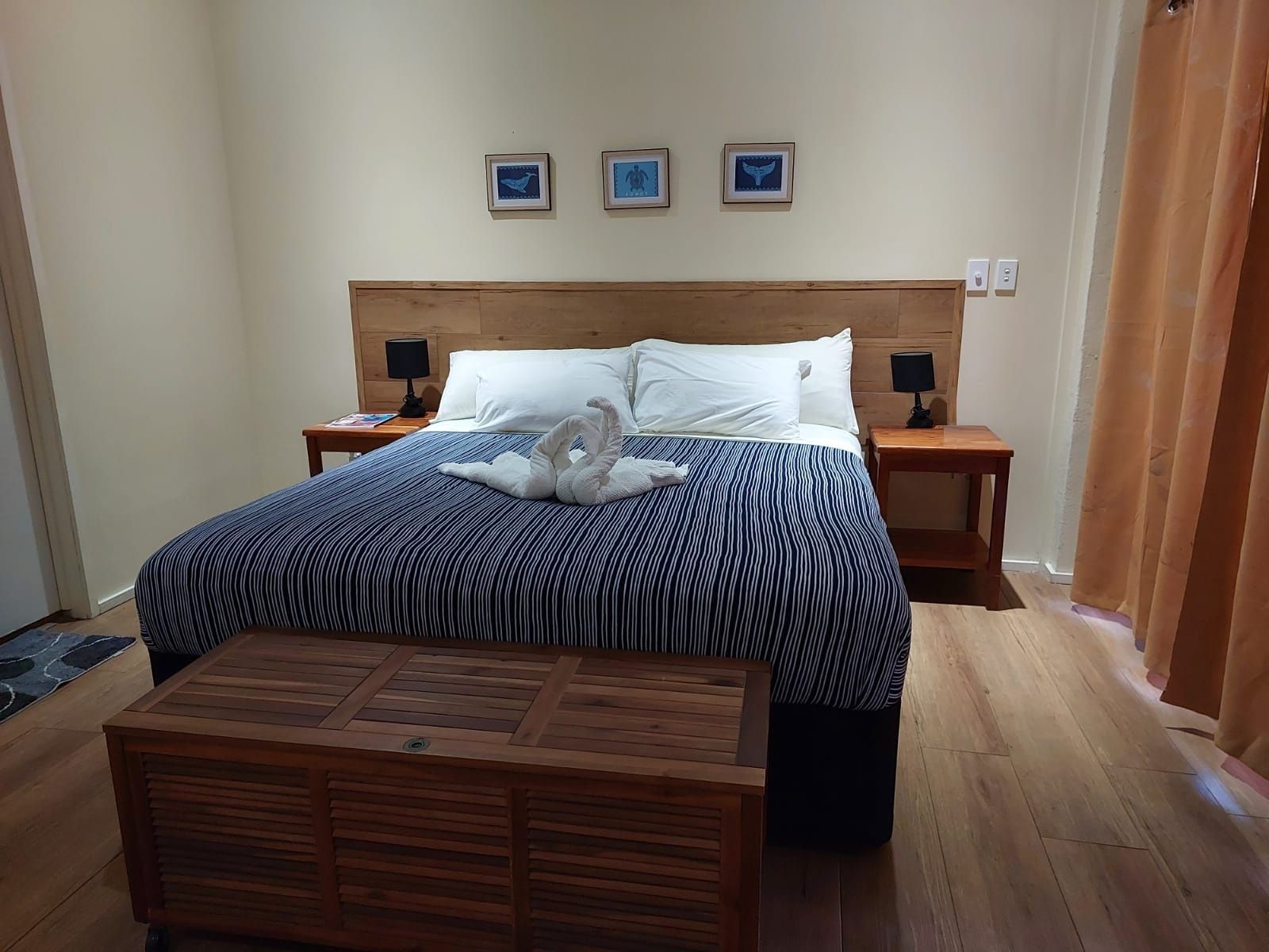 A hotel room with a wooden headboard, a bed with striped bedding, two bedside tables with lamps, and a wooden bench at the foot of the bed.