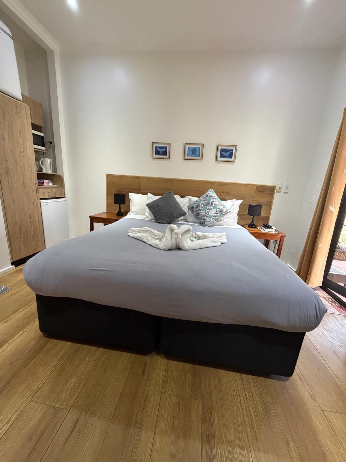 A hotel room with a large bed, wooden flooring, a wardrobe, and a small table with a lamp.