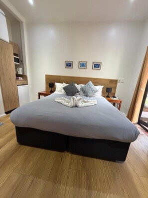 A hotel room with a large bed, wooden flooring, a wardrobe, and a small table with a lamp. - Winnies B&B (Nuku'alofa)