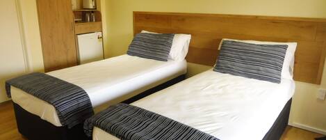 Dos camas individuales con ropa de cama a rayas, un cabecero de madera, una pequeña kitchenette con microondas y un armario de madera.