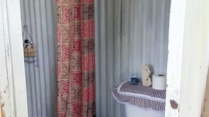 Ein kleines, abgeschlossenes Badezimmer mit einer gemusterten Duschvorhang, einer Toilette mit kariertem Sitz und einem Metallregal mit einem Handtuch.