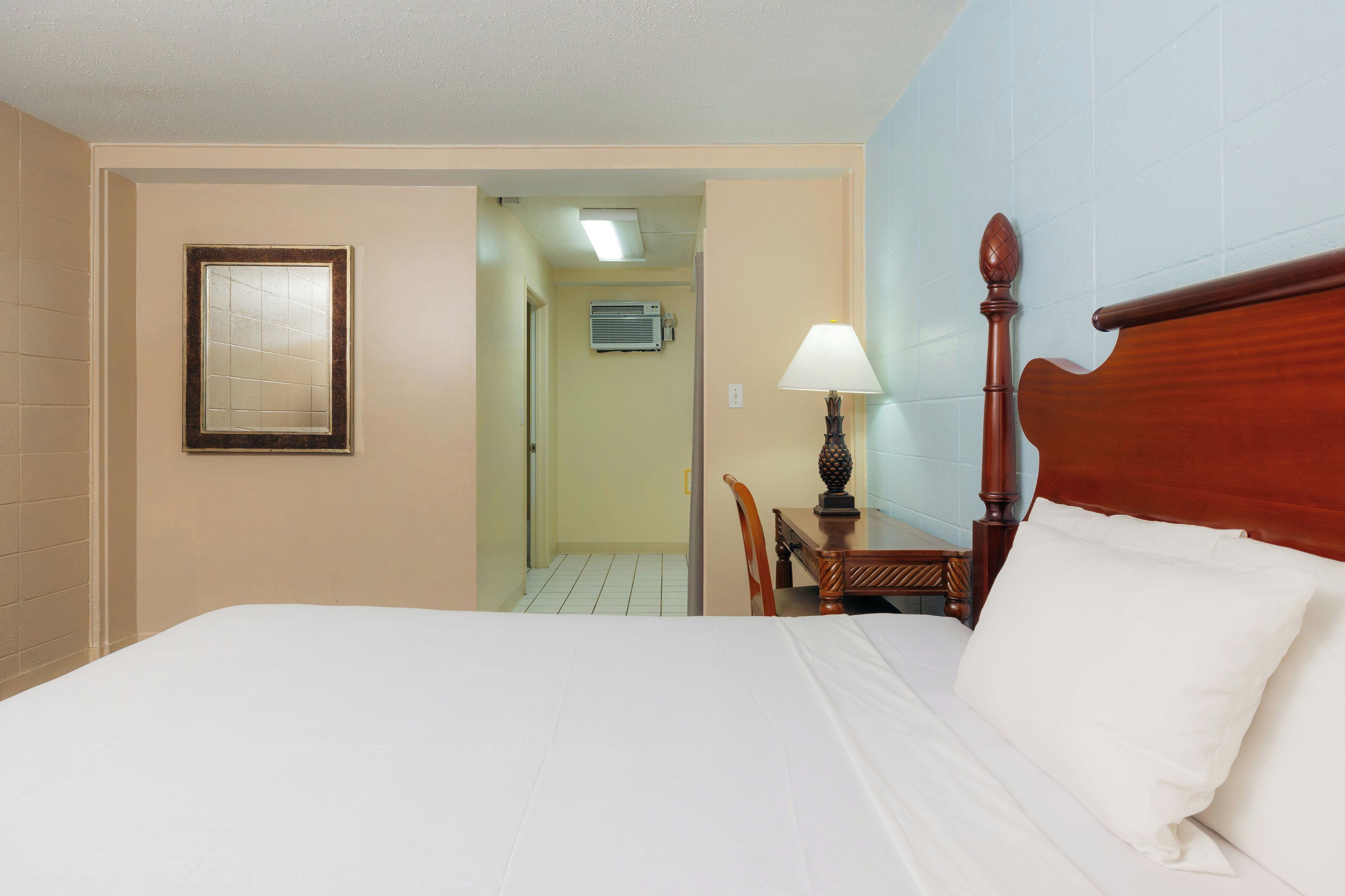 Une chambre d’hôtel avec un lit, une chaise, un bureau, une lampe et un cadre photo.