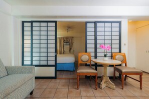 Habitación de hotel con cama, sofá, mesa de comedor con sillas y puerta corrediza con vistas.