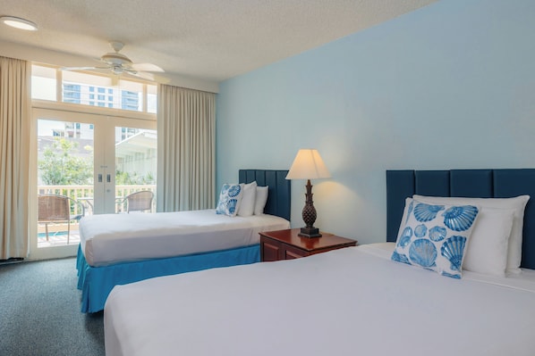 Habitación de hotel con dos camas, ventilador de techo, ventana con cortinas y vista al exterior.