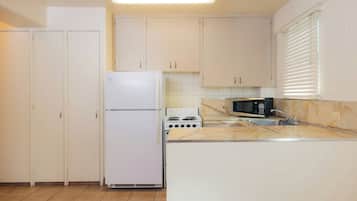 A compact kitchen with white cabinets, a refrigerator, a stove, and a microwave.