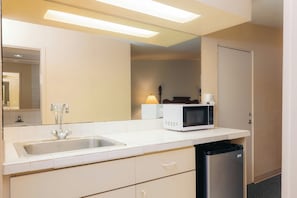 Una kitchenette compacta con un lavamanos, un microondas y un pequeño bote de basura.