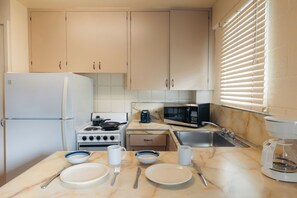 A compact kitchen with white cabinets, a stove, microwave, and a sink.
