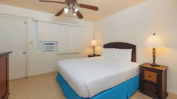 A bedroom with a bed, two bedside lamps, a ceiling fan, a window with blinds, and a radiator.