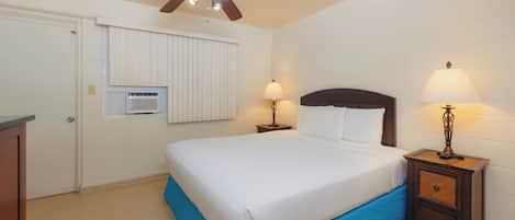 A bedroom with a bed, two bedside lamps, a ceiling fan, a window with blinds, and a radiator.