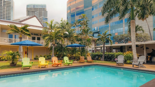 Una piscina con múltiples sillones de descanso y sombrillas, rodeada de palmeras y edificios modernos.