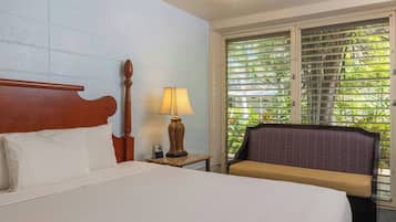 A hotel room with a bed, a bedside lamp, a telephone, and a window with a view of greenery.