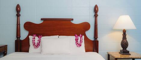 A bed with a wooden headboard, white bedding, and a lei on the pillows.