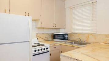 A compact kitchen with white cabinets, a white refrigerator, a stove, a microwave, and a sink.