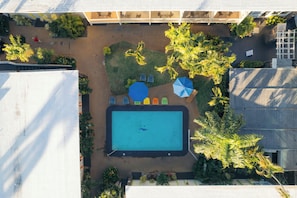 An aerial view of a rooftop swimming pool with surrounding lounge chairs and umbrellas. - Waikiki Heritage Hotel (Honolulu)