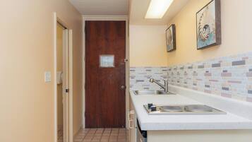 Un pasillo estrecho que lleva a una puerta de madera, una cocina con salpicadero de azulejos y un lavamanos.