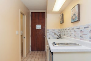 A narrow hallway leading to a wooden door, a kitchen with a tiled backsplash, and a sink. - Waikiki Heritage Hotel (Honolulu)