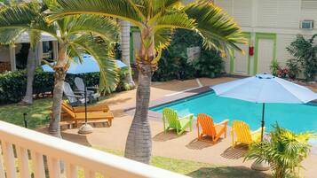 A pool area with lounge chairs, umbrellas, and palm trees.