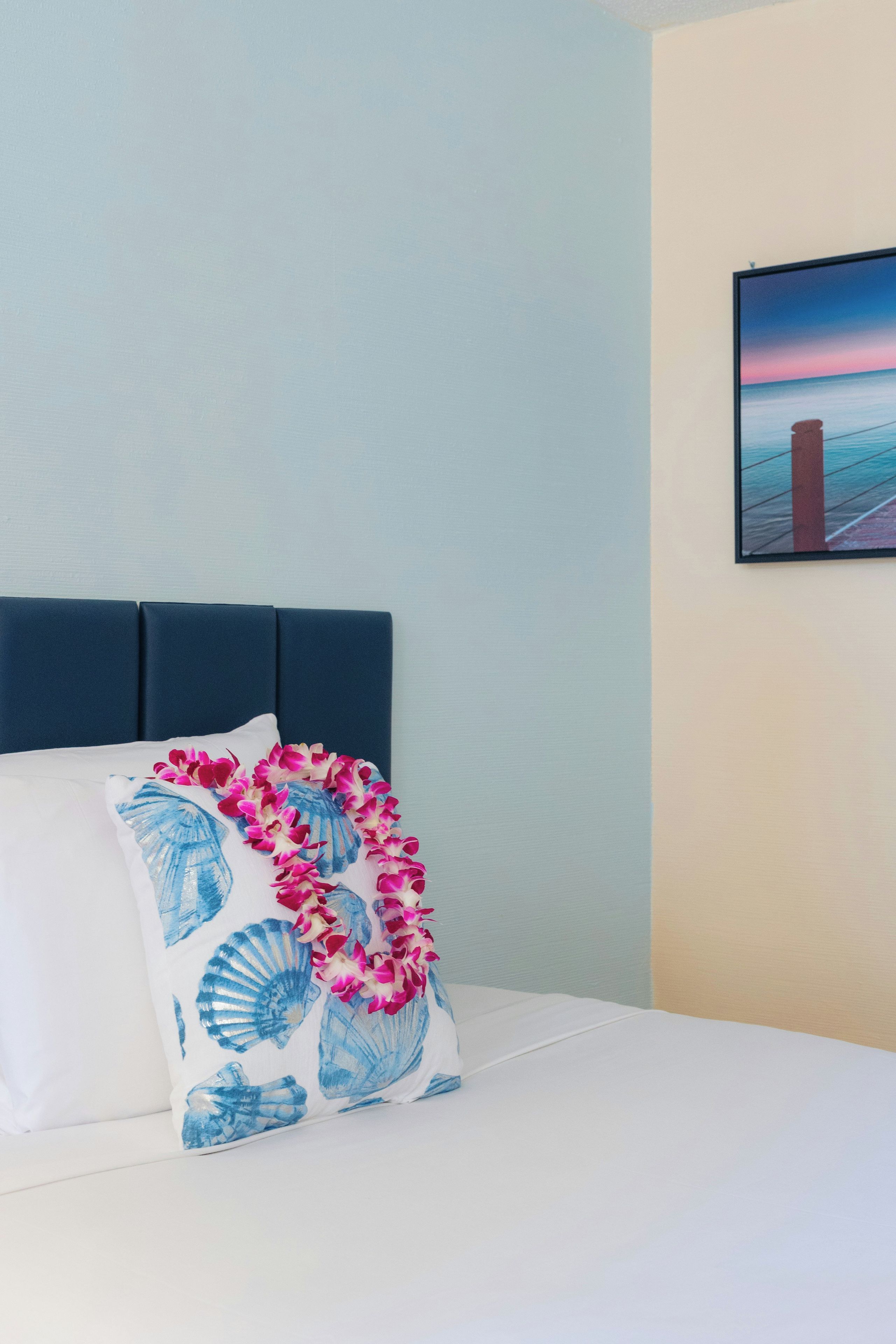 A bed with a blue headboard, white bedding, and a floral pillow.