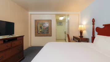 Habitación de hotel con cama, televisión, escritorio con cajones, un cuadro en la pared, lámpara y una silla.