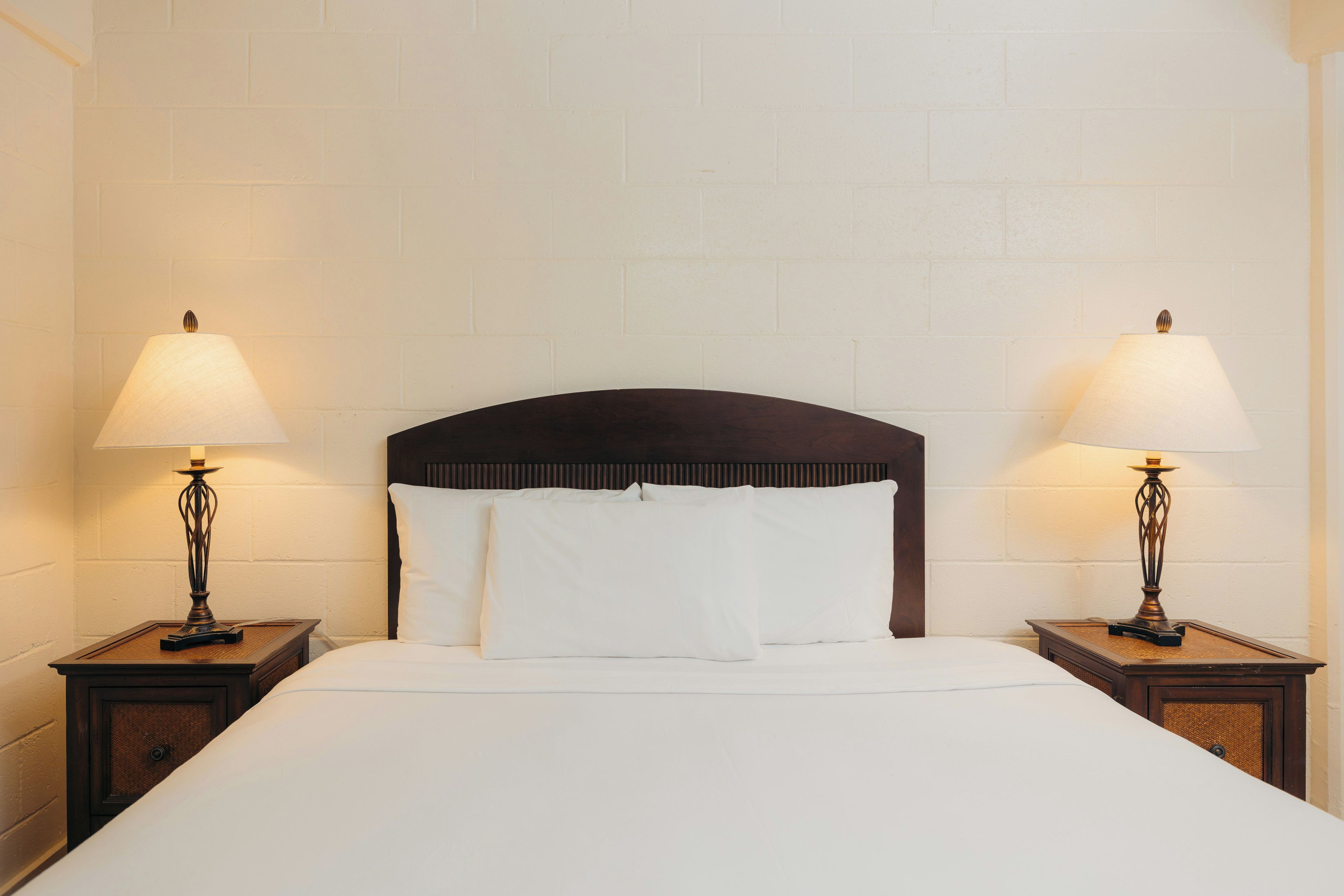 A hotel room with a large bed, two bedside tables with lamps, and a plain brick wall.